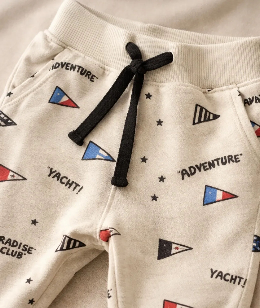 Pantaloncito de algodón para bebé, color crudo con estampa de banderines náuticos y estrellas. Tiene cordón ajustable en la cintura y puños elastizados. Ideal para el día a día o para un look canchero.