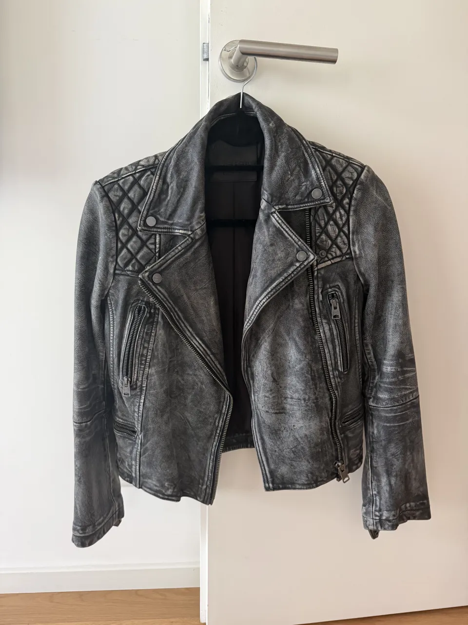 Campera de cuero gris con detalles acolchados en los hombros y cierres metálicos. Posee cuello solapa y puños con cierre.