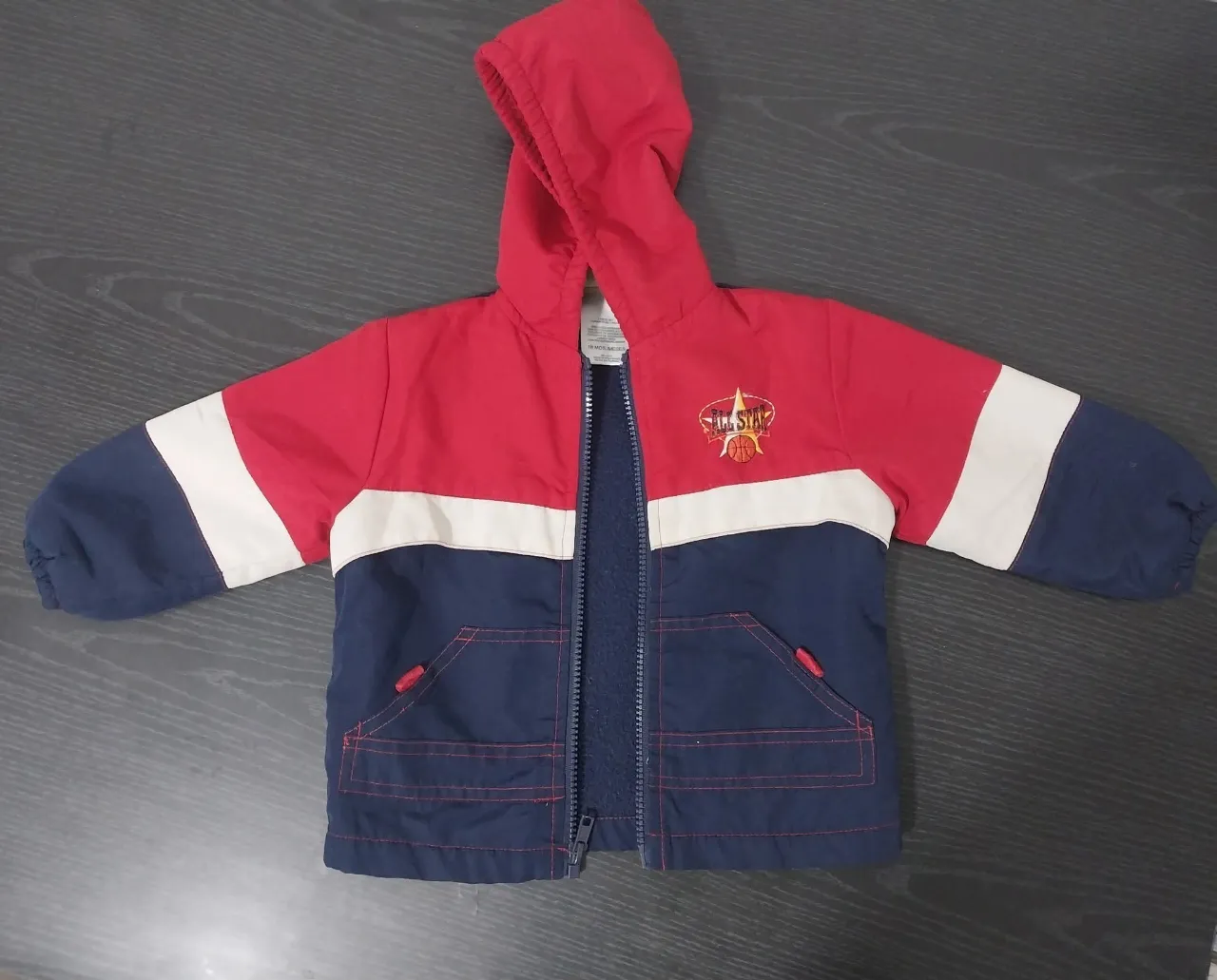 Campera infantil con capucha, cierre al frente y bolsillos laterales. Diseño tricolor con detalles de bordado en el frente.