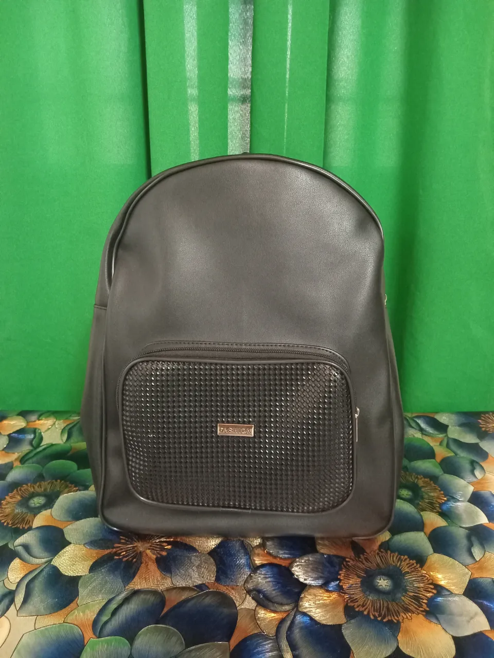 Mochila negra con bolsillo frontal texturizado y logo metálico. Cierre principal y correas ajustables.