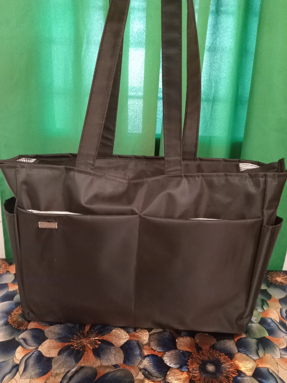 Bolso negro grande con dos bolsillos frontales y dos laterales. Interior forrado a rayas con divisiones.