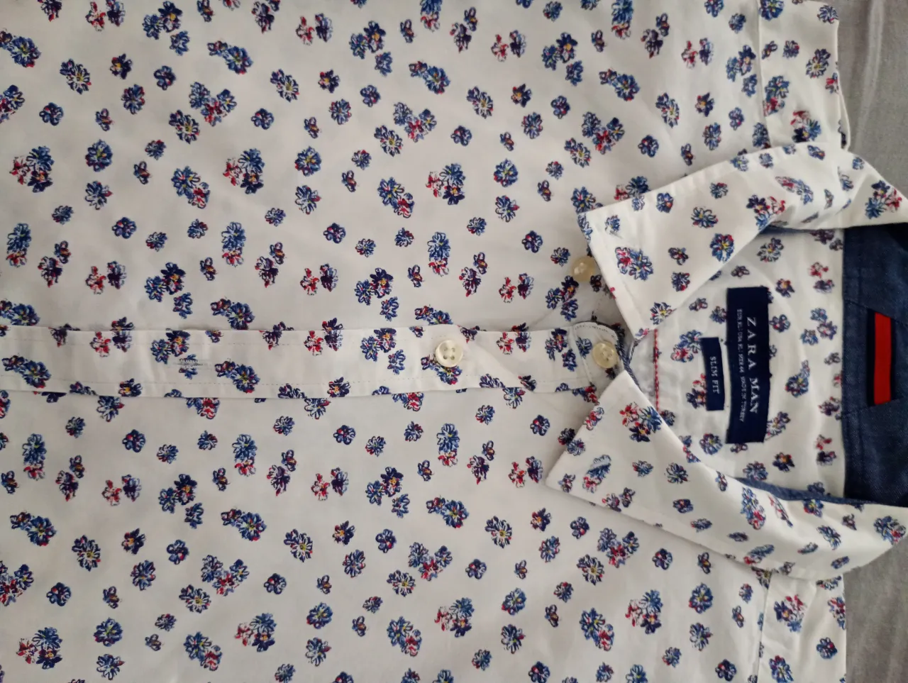 Camisa de jean con botones al frente. Posee cuello y un bolsillo en el frente. La otra camisa es blanca con estampa de flores en tonos azules y rojos.