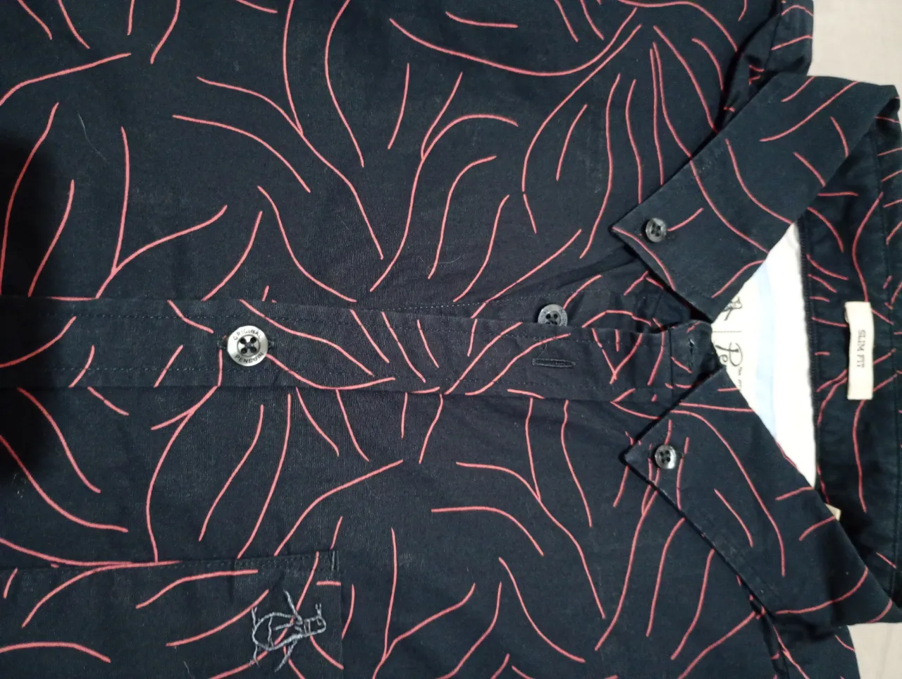 Camisa estampada con diseño de hojas tropicales en fondo azul marino. Posee cuello camisero, manga corta y botones al frente.