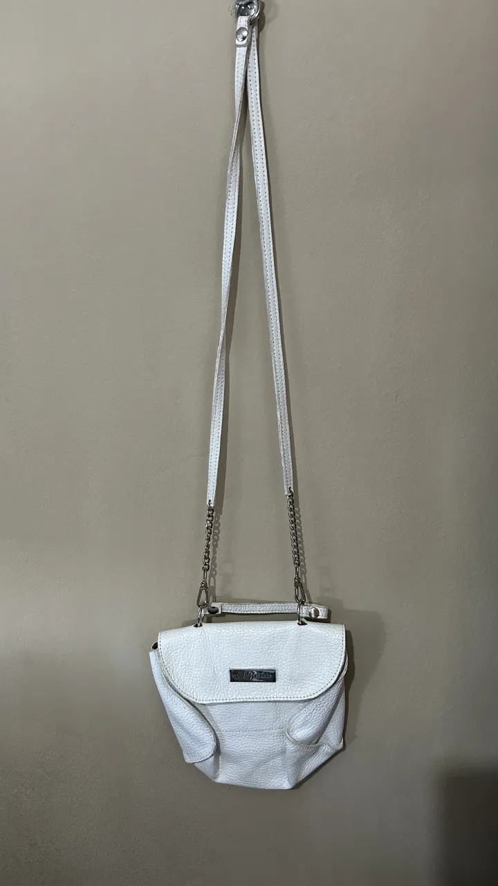 Cartera blanca con correa larga y detalles de cadena. Posee un bolsillo exterior con cierre.. Es de Cuero! súper hermosa, combina con todo!!
