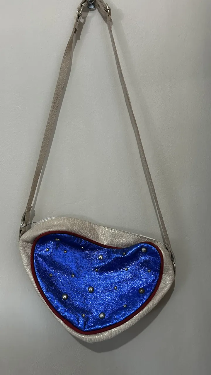 Bolso con forma de corazón, de cuero vacuno.
Beige dorado, texturizado y aplique central azul metálico con tachas. hermoso!!! 