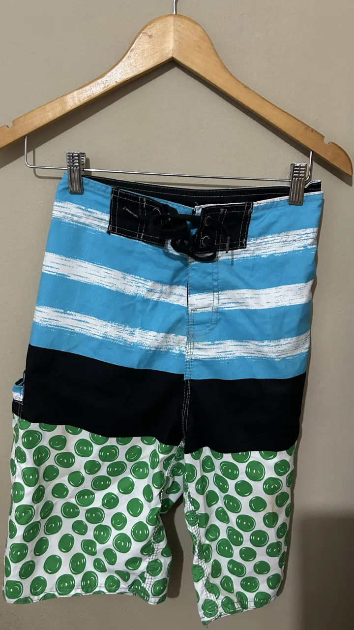 Short de baño con franjas horizontales celestes y blancas en la parte superior, seguido de una franja negra y un estampado de círculos verdes sobre fondo blanco en la parte inferior. Posee cordones para ajustar en la cintura. poco uso! cómo nueva! 