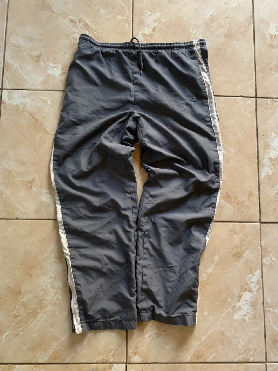 Pantalon de entrenamiento gris con detalles blancos en los laterales. Ideal para entrenar o para un look casual y cómodo.