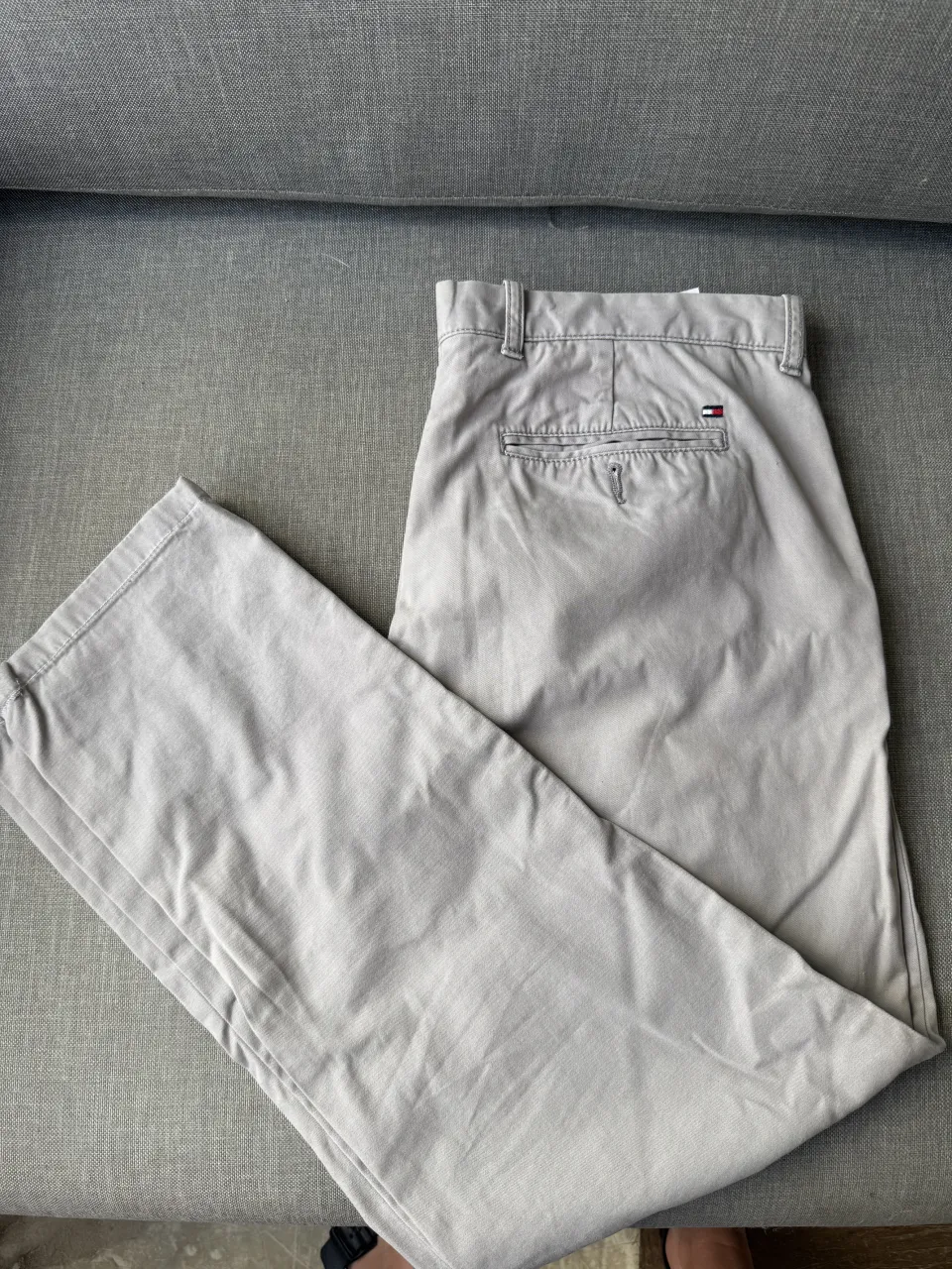 Pantalón de gabardina color gris claro. Tiene bolsillos traseros y un pequeño logo de la marca en uno de ellos.