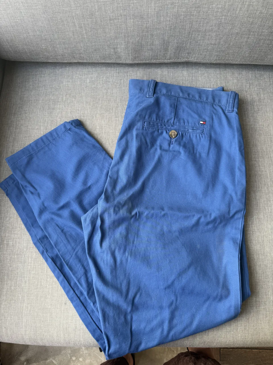Pantalón de gabardina azul con dos bolsillos traseros, uno con botón. Posee etiqueta interna de la marca Tommy Hilfiger y detalle de talle 34/30. Custom Fit