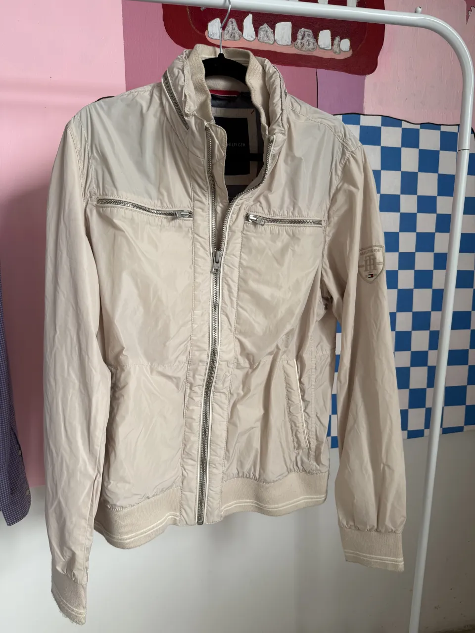 Campera Tommy Hilfiger color crudo con cierre completo y cuello alto. Posee bolsillos con cierre en el frente y un logo bordado en la manga izquierda.