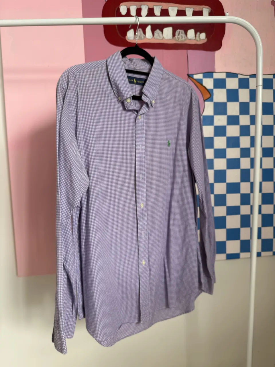 Camisa Polo a cuadros de manga larga color lila y blanco. Tiene cuello con botones y un pequeño logo bordado en el frente.