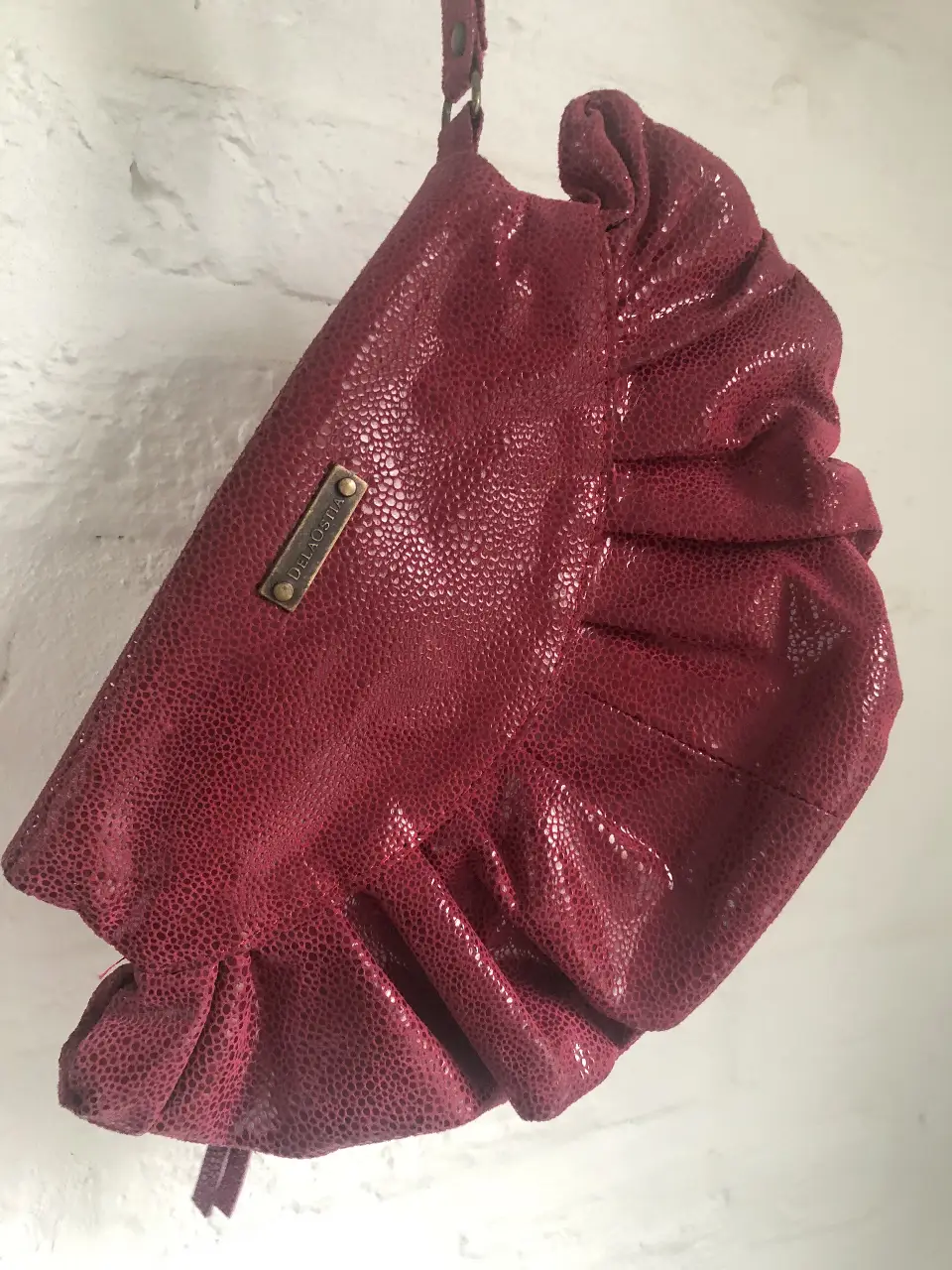 Cartera de mano de cuero roja con textura símil piel de reptil y detalle de volados. Ideal para eventos y salidas.