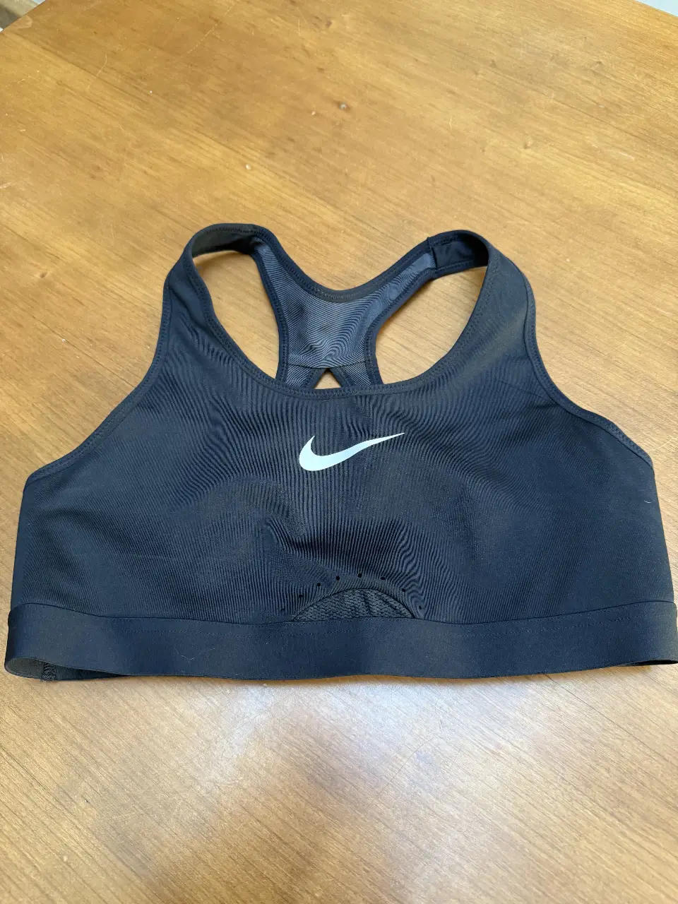 Corpiño deportivo Nike negro, ideal para actividades de alto impacto. Confeccionado con materiales de alta calidad para brindar soporte y comodidad. Logo de la marca en blanco.