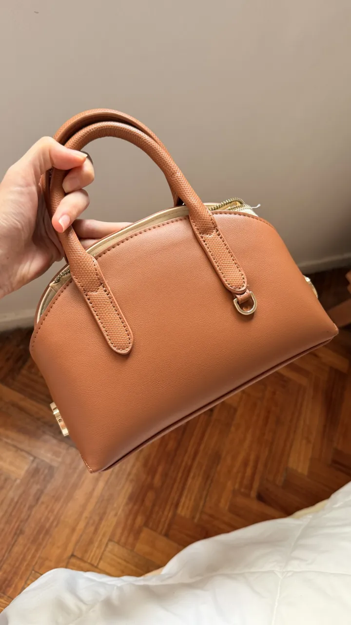 Bolso marrón de cuero sintético con manijas cortas y correa de hombro tejida desmontable. Cierre superior con detalle de herrajes dorados. Comprada en Italia.