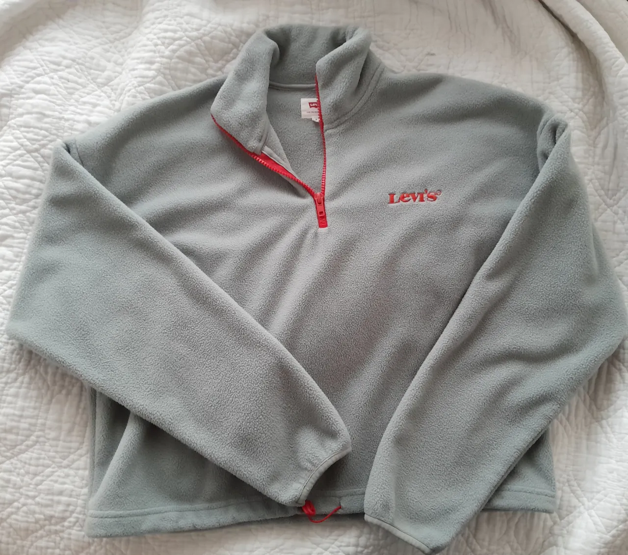 Buzo gris de polar con cierre rojo al cuello y logo de Levi's bordado en rojo en el frente.