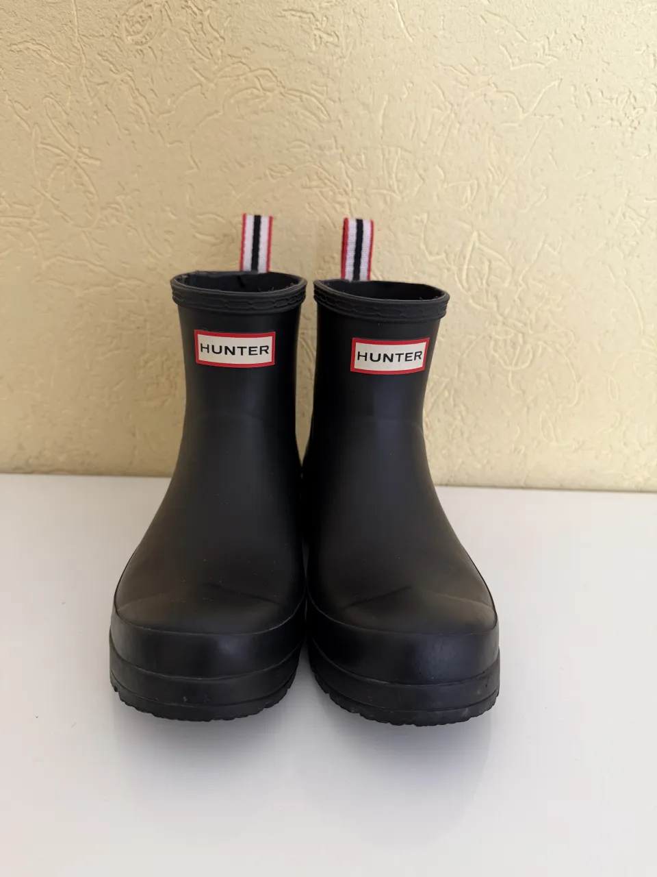 Botas de lluvia negras de caña baja con tiras a rayas rojas, blancas y negras en la parte superior. 