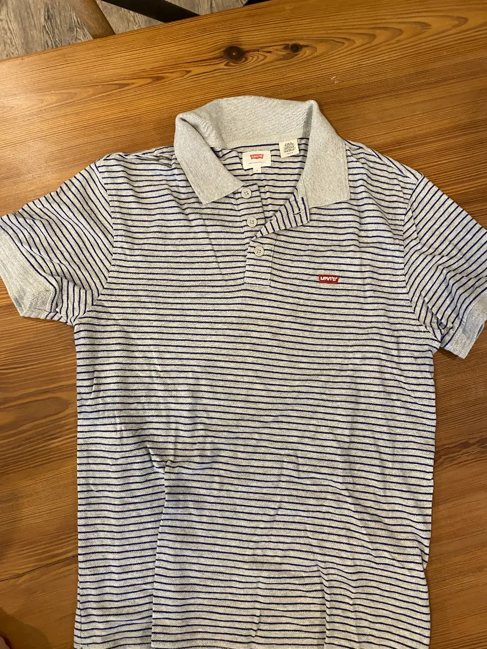 Remera polo de hombre a rayas grises y azules, con cuello y mangas en gris. Marca Levi's, talle S.