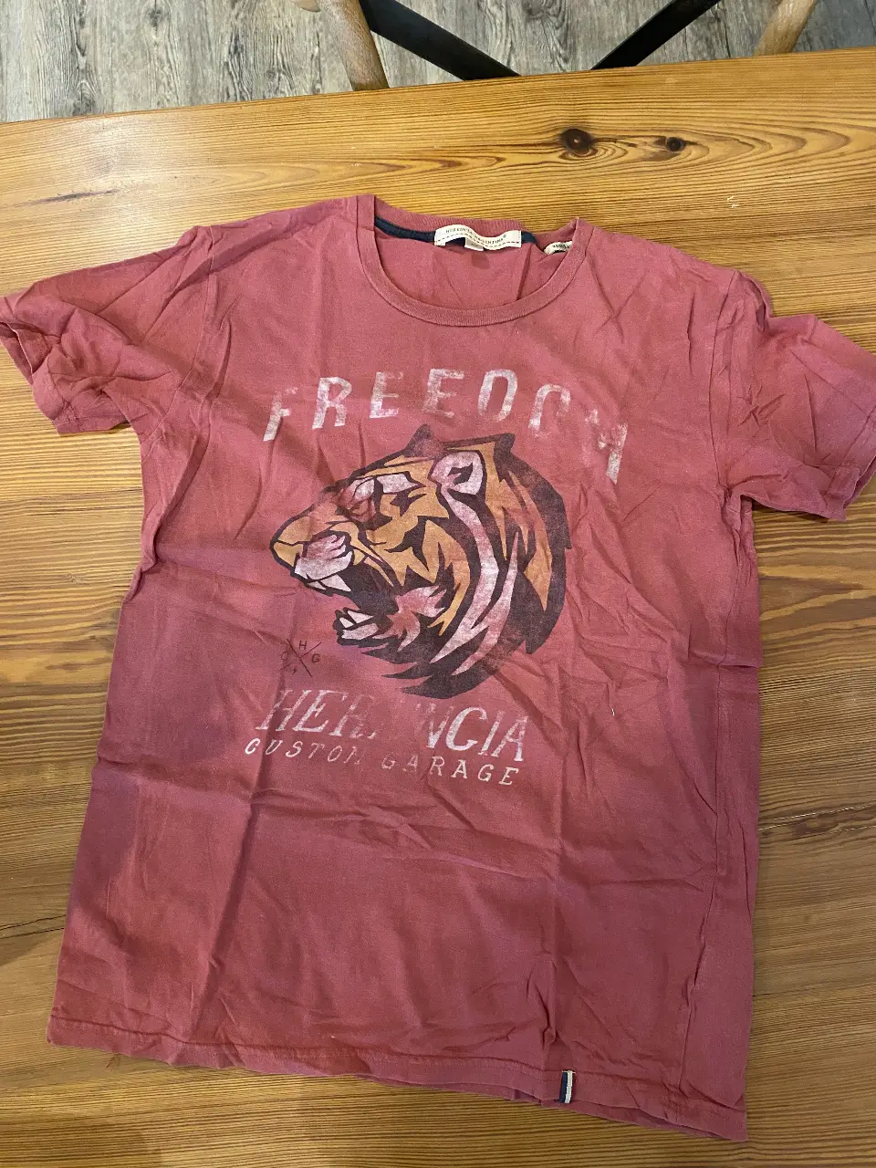 Remera de hombre de color bordó con estampado de tigre y la frase "FREEDOM" en la parte delantera. Marca "HERENCIA ARGENTINA CUSTOM GARAGE". Ideal para un look casual y con onda.