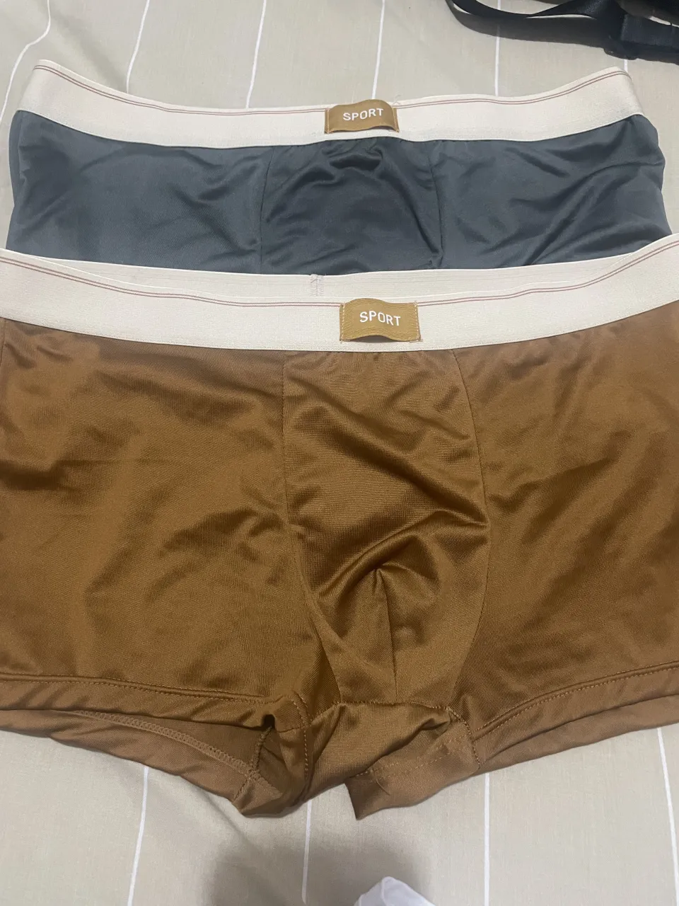 Pack de dos boxers de hombre. Uno gris oscuro y otro marrón. Ambos con elástico blanco en la cintura y etiqueta con la palabra "SPORT".
