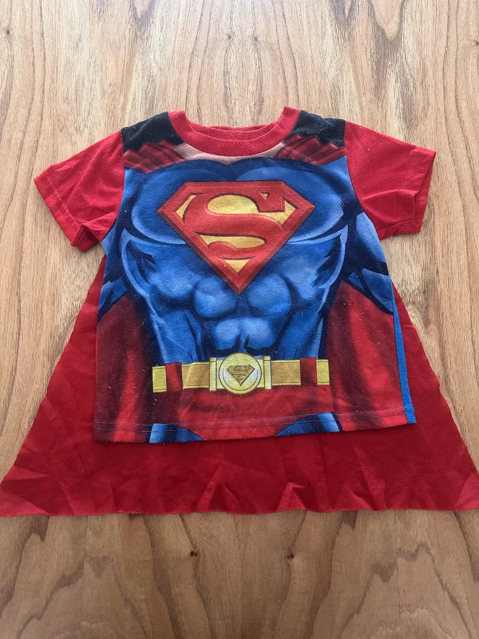 Disfraz de Superman para niños, incluye remera con diseño del traje y capa roja. Ideal para fiestas y juegos.
