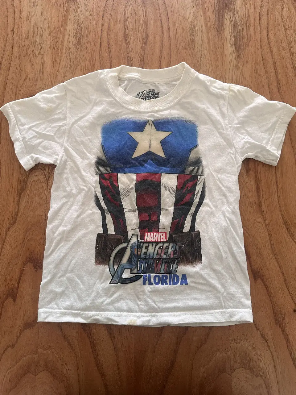 Remera blanca de manga corta para niño con estampado de Capitán América y el logo de Avengers. Ideal para fanáticos de Marvel y para un look casual y divertido.