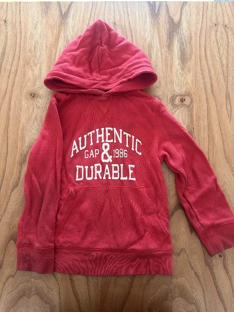 Buzo canguro rojo de la marca GAP, con capucha y bolsillo delantero. Estampado "AUTHENTIC GAP & 1986 DURABLE" en blanco. Ideal para un look casual y cómodo.