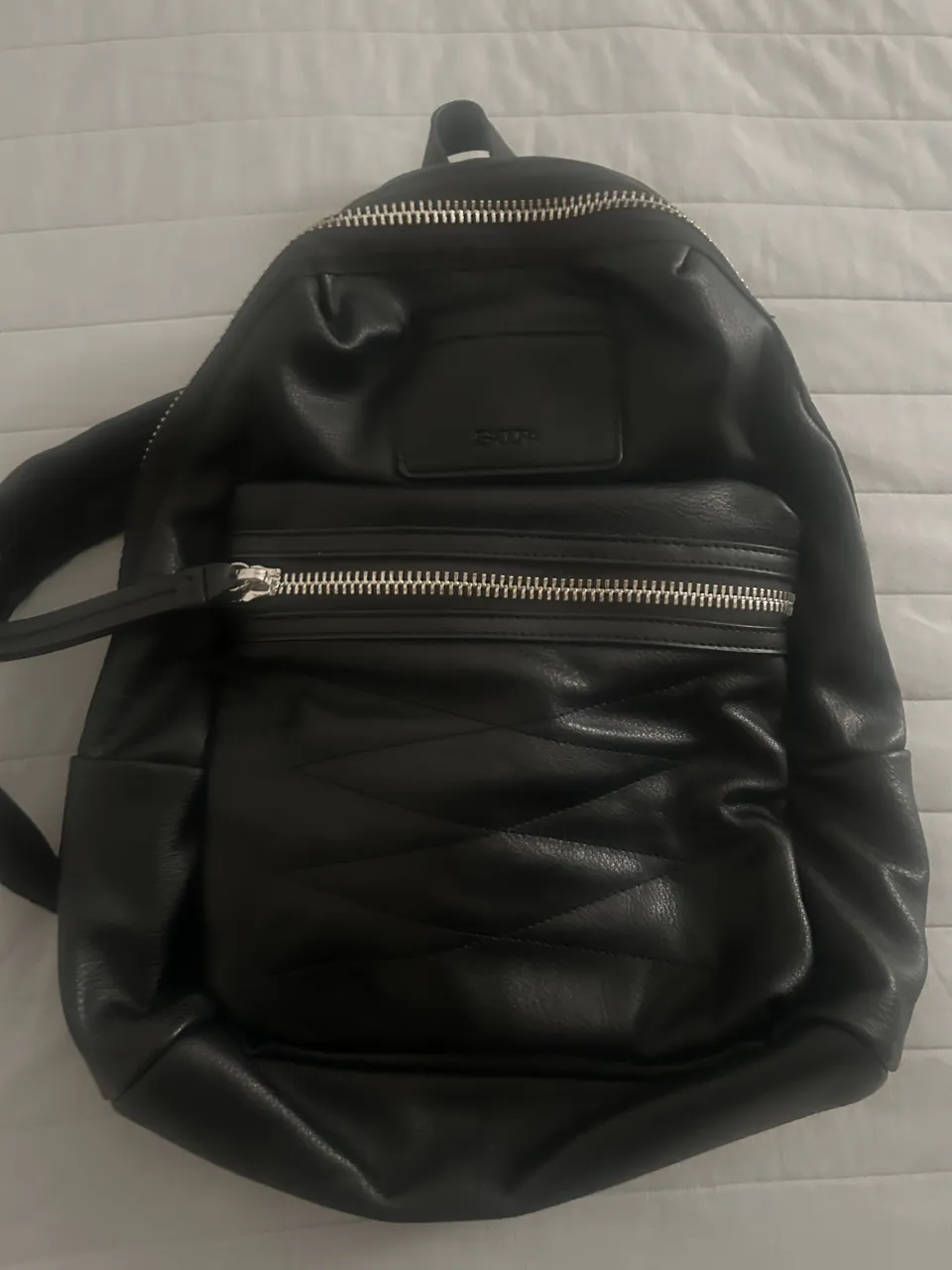 Mochila negra de cuero sintético, con múltiples bolsillos frontales y detalles acolchados. Ideal para el día a día o para llevar tus esenciales con estilo.