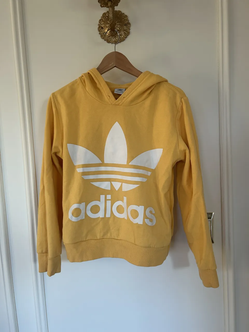 Buzo amarillo con capucha y logo de Adidas estampado en blanco en el frente.
