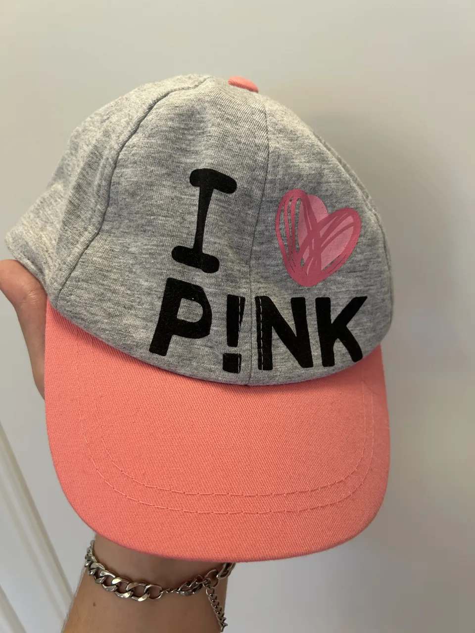 Gorra de algodón gris con visera de color rosa. Estampado frontal "I P!NK" con un corazón rosa.