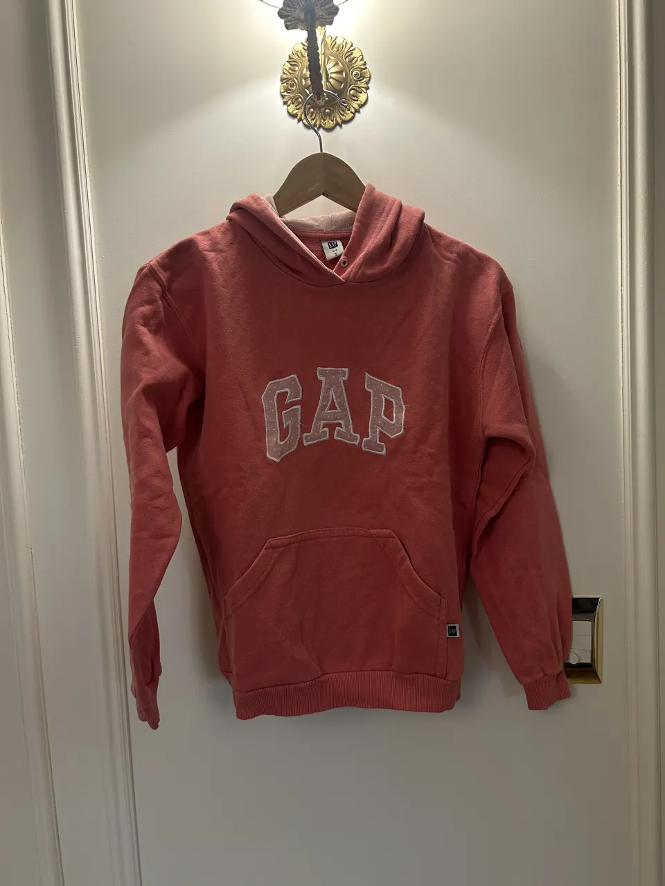 Buzo con capucha de color salmón, con logo de la marca bordado en el frente. Posee bolsillo canguro.