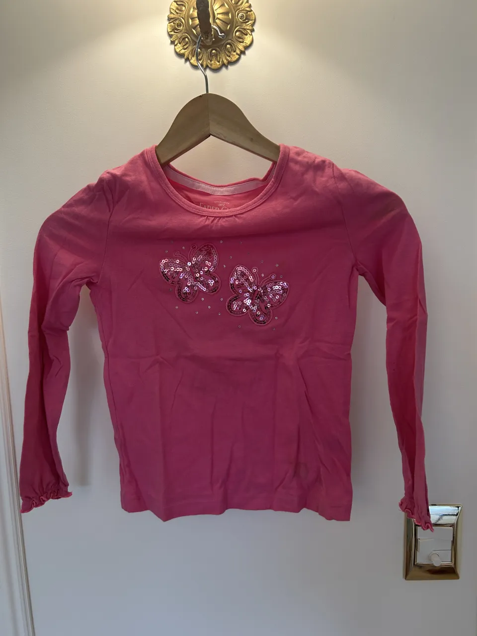 Remera manga larga de algodón orgánico color rosa. Posee dos mariposas bordadas con lentejuelas y detalles brillantes en el frente. 