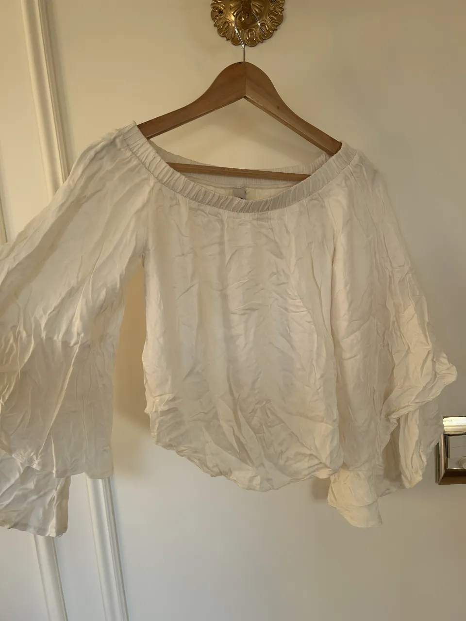 Blusa blanca con mangas acampanadas y escote elástico. Detalle de volados en las mangas.