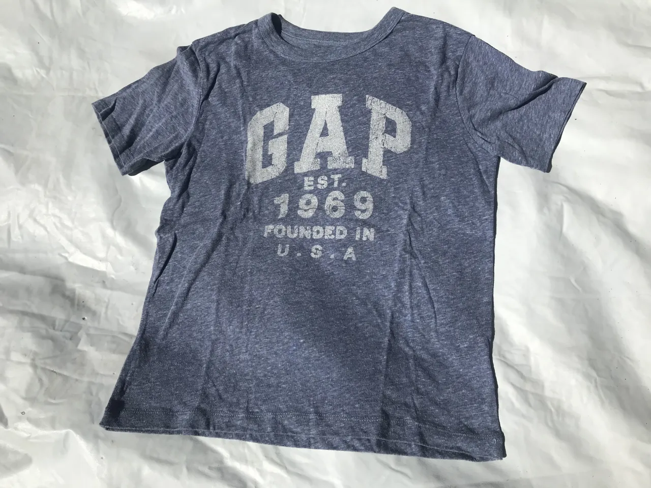 Remera azul de manga corta con estampa "GAP est. 1969 FOUNDED IN U.S.A." en blanco en el frente.