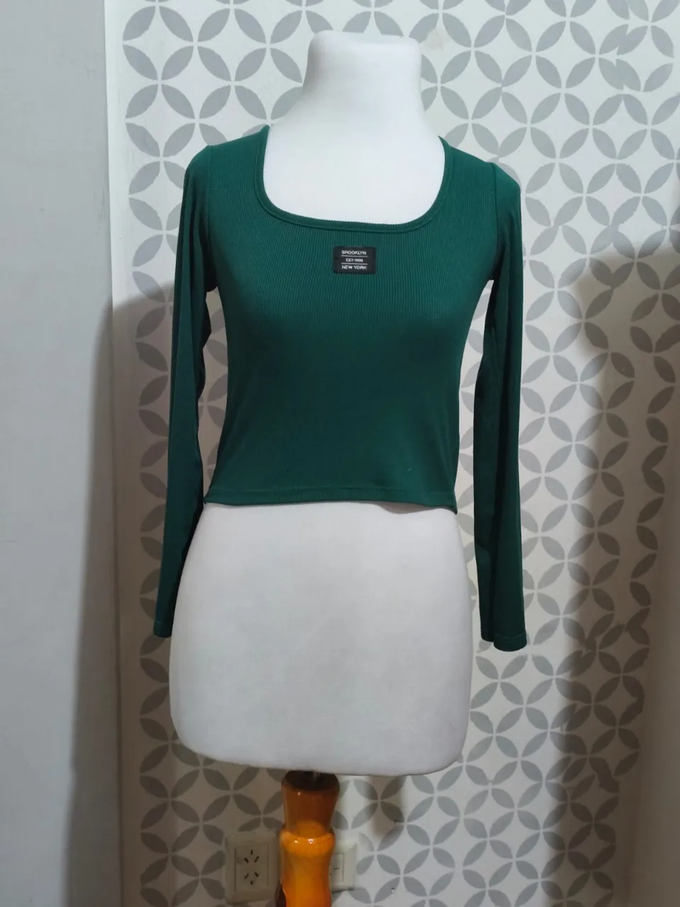 Remera manga larga verde oscuro, con escote cuadrado y detalle de etiqueta "BROOKLYN EST. 1990 NEW YORK" en el frente. Un básico canchero para tu día a día.