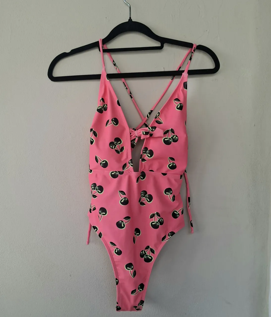 ¡Llamá la atención con este traje de baño súper canchero! De color rosa vibrante y con un estampado de cerezas negras que te va a enamorar. Tiene un diseño cruzado en el frente con un moño y un corte sutil en la cintura. Las tiras se cruzan en la espalda, dándole un toque súper sexy. ¡Ideal para lucirte en la playa o la pileta!