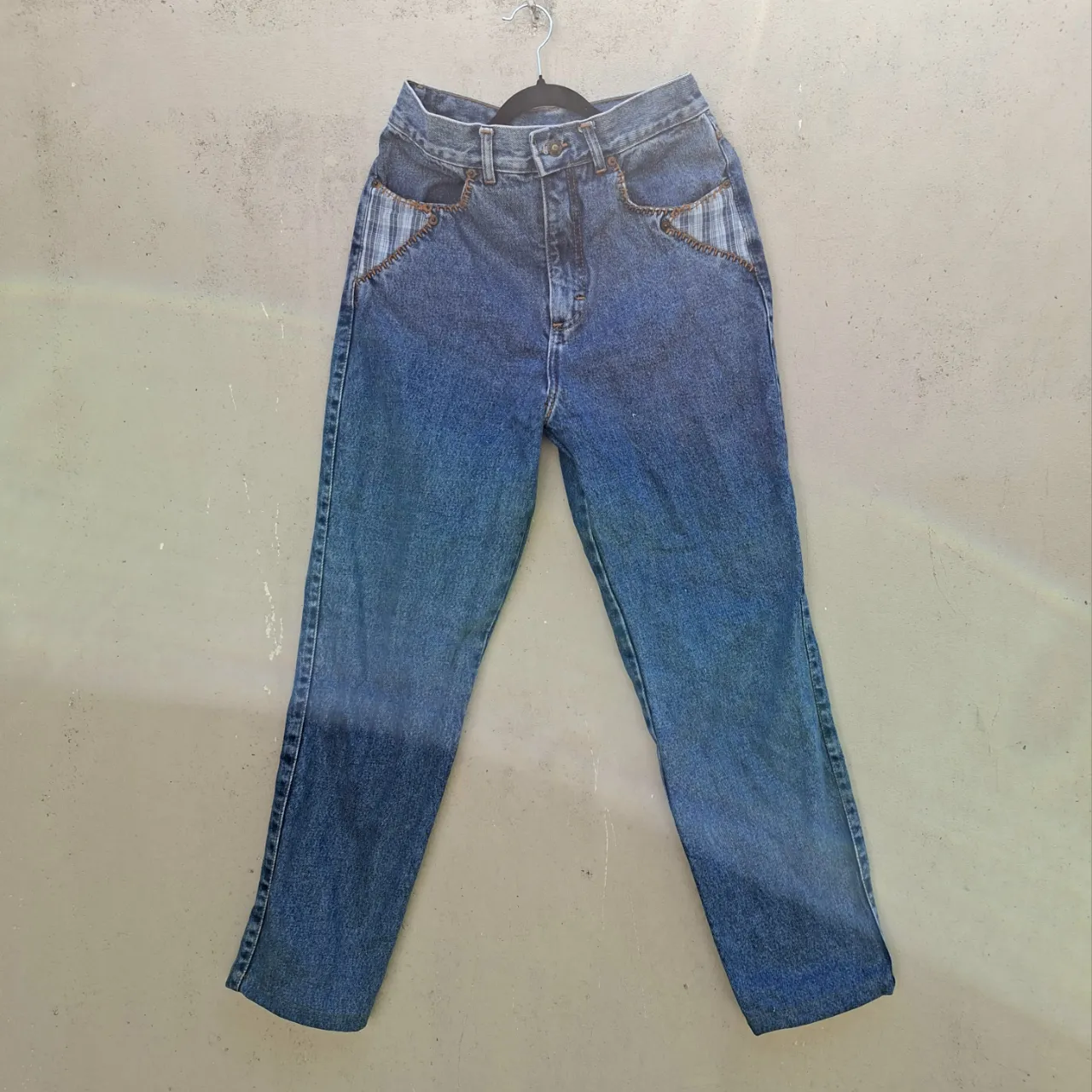¡Jeans vintage tiro alto con un toque único! Estos jeans de corte recto son perfectos para un look casual y canchero. Tienen detalles de tela a cuadros en los bolsillos delanteros y costuras a la vista que le dan un estilo original. El degradado en las piernas añade un toque moderno. Ideales para combinar con remeras o buzos.