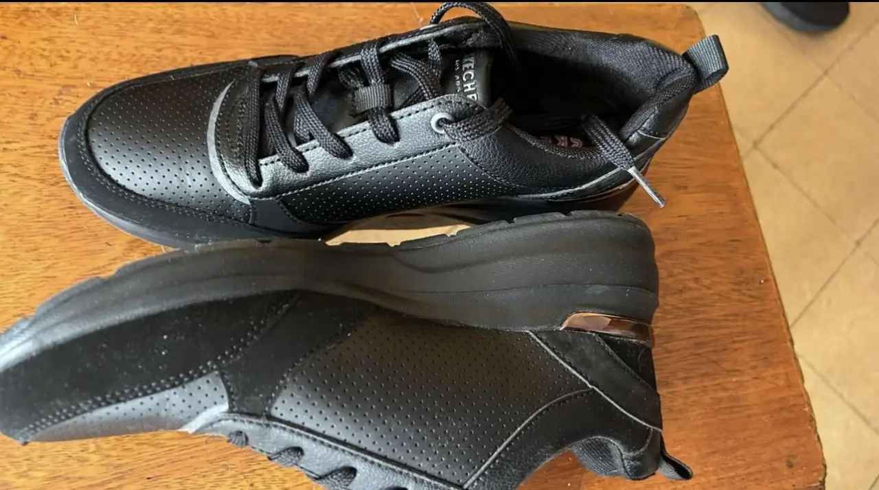 Zapatillas Skechers negras para mujer, con diseño moderno y plataforma sutil, detalles dorados. Ideales para uso diario, combinan estilo y comodidad.