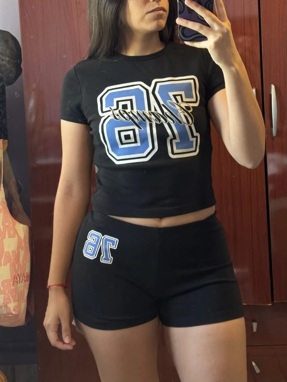 Conjunto deportivo negro de remera manga corta y shorts. La remera tiene un estampado grande en el frente con el número "76" en azul y blanco. Los shorts son negros con el mismo estampado en la parte inferior izquierda.