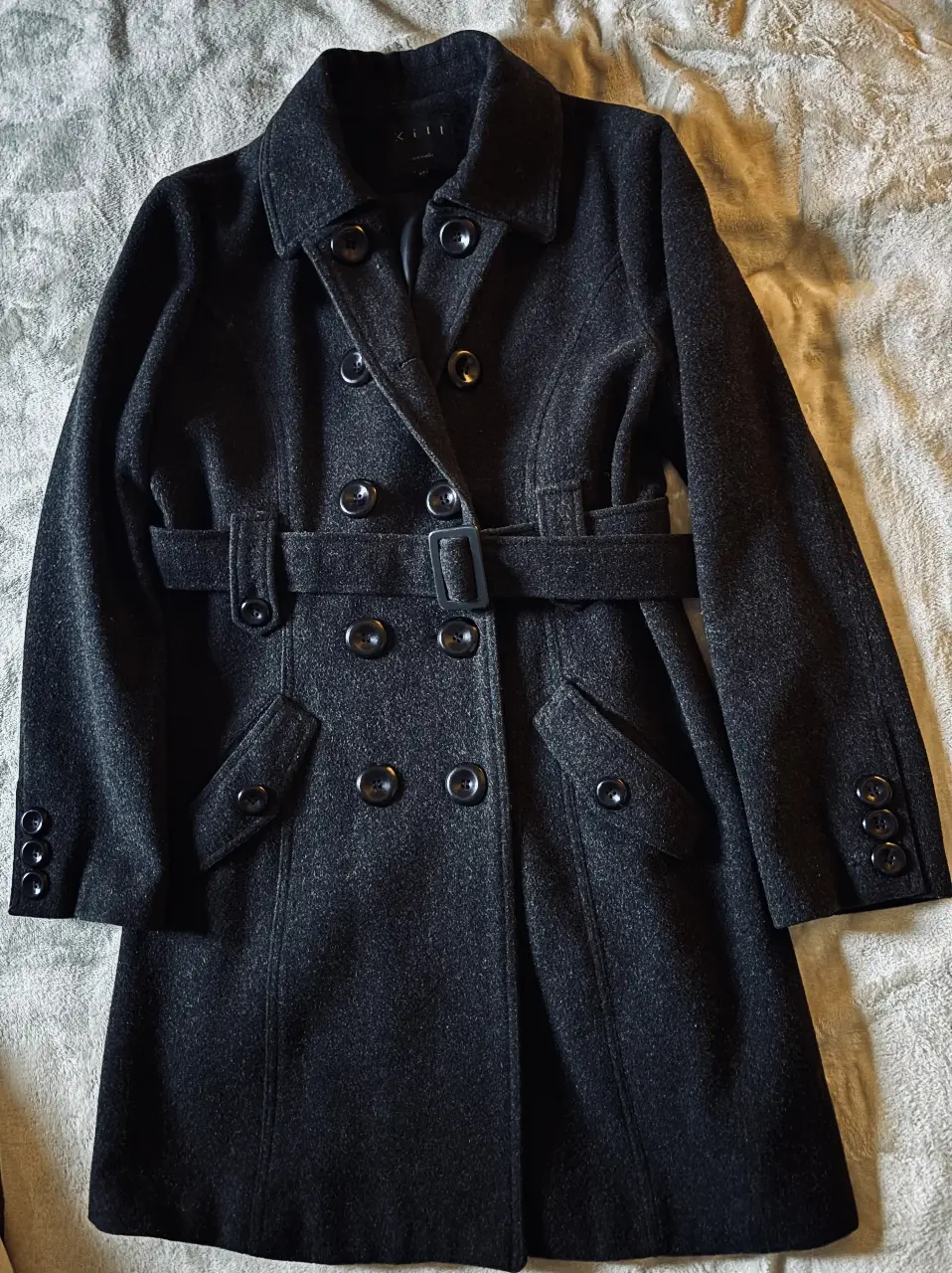 Tapado largo de paño gris oscuro con cinturón. Posee botones y bolsillos delanteros. Ideal para un look elegante y abrigado en invierno.