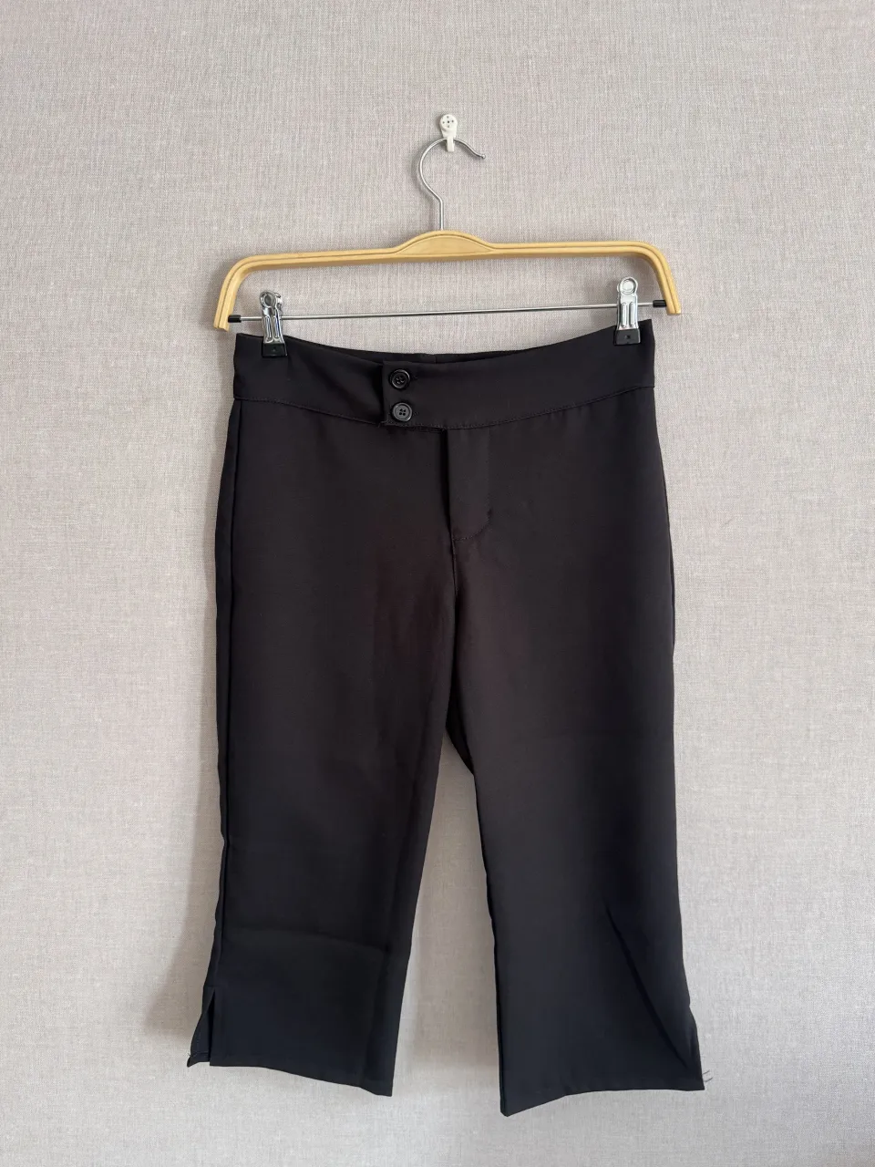 Pantalón negro con dos botones en la cintura y tajos en los bajos.