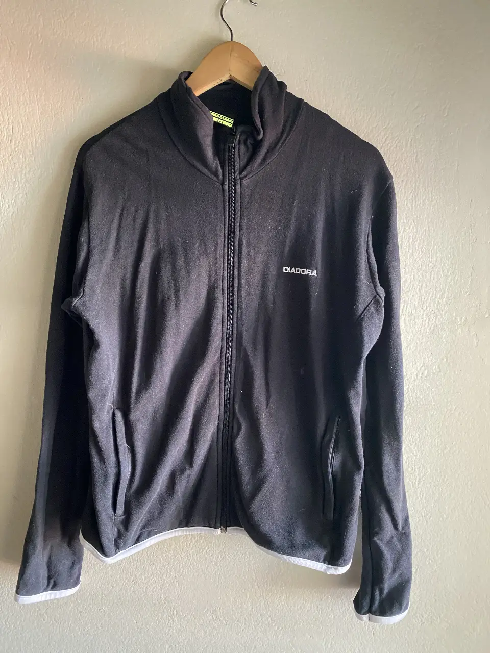 Buzo deportivo con cierre y cuello alto de la marca Diadora. Color negro con detalles blancos en los bordes. Talle M.