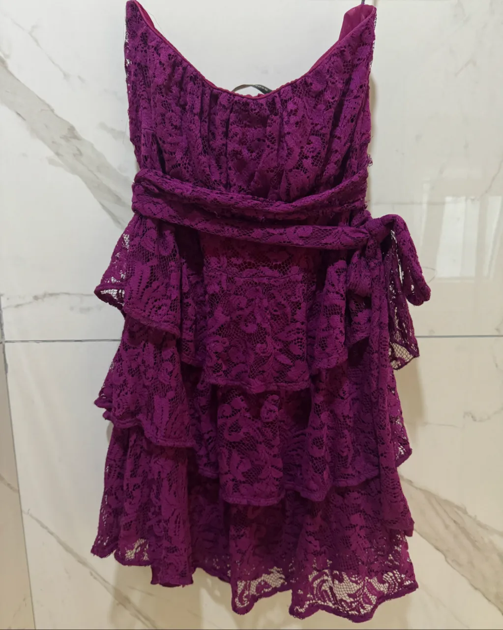 Vestido corto de encaje morado con volados en la falda y lazo en la cintura.