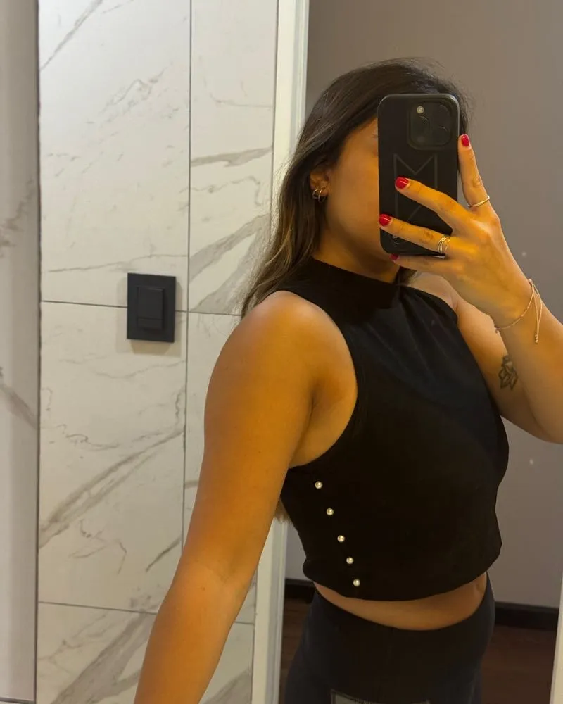 Top negro de cuello alto sin mangas, con detalle de botones nacarados en el lateral. Un diseño moderno y elegante, perfecto para combinar con tus outfits.