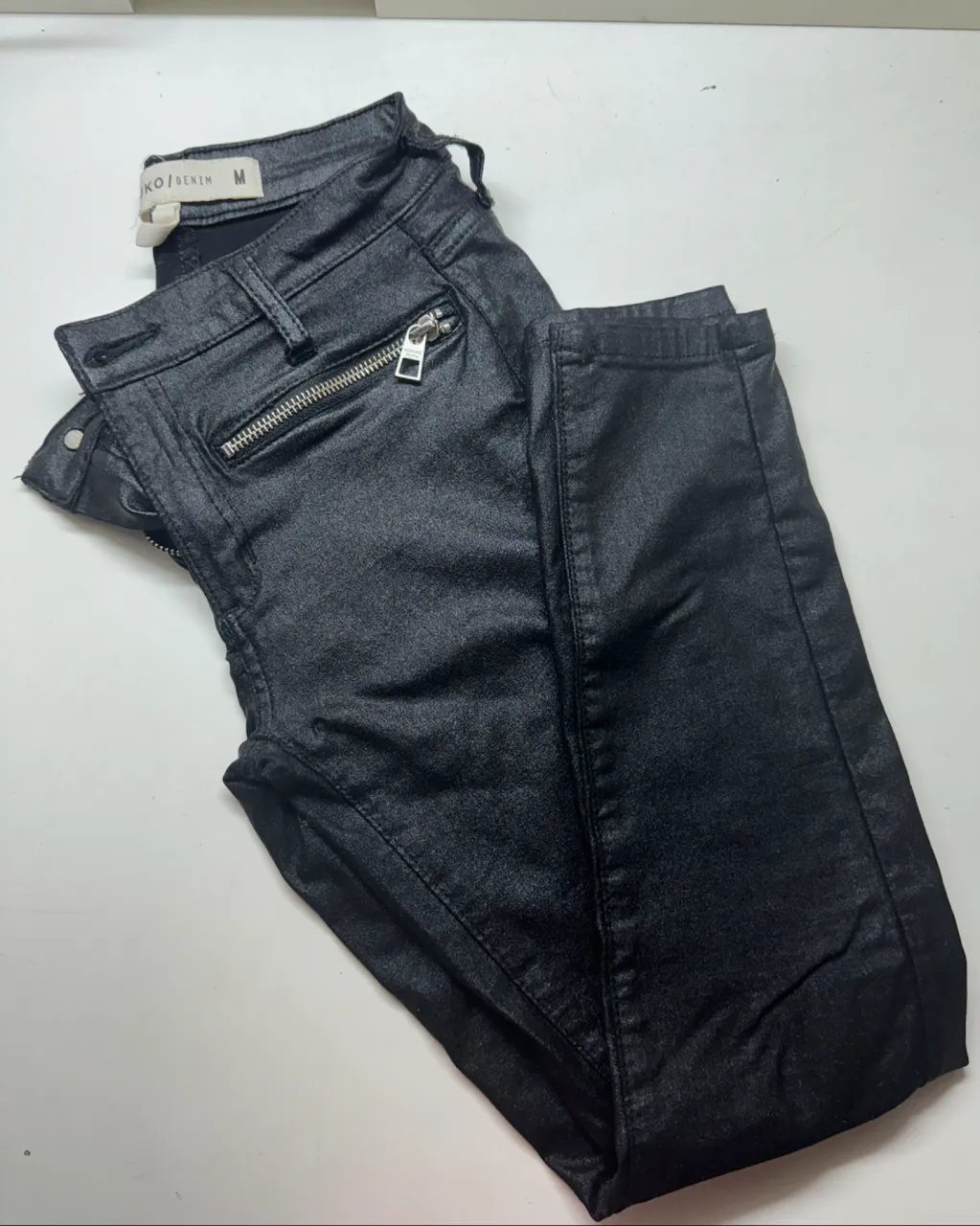 Pantalón de jean negro con detalles de cierres metálicos en los bolsillos delanteros. Posee bolsillos traseros.