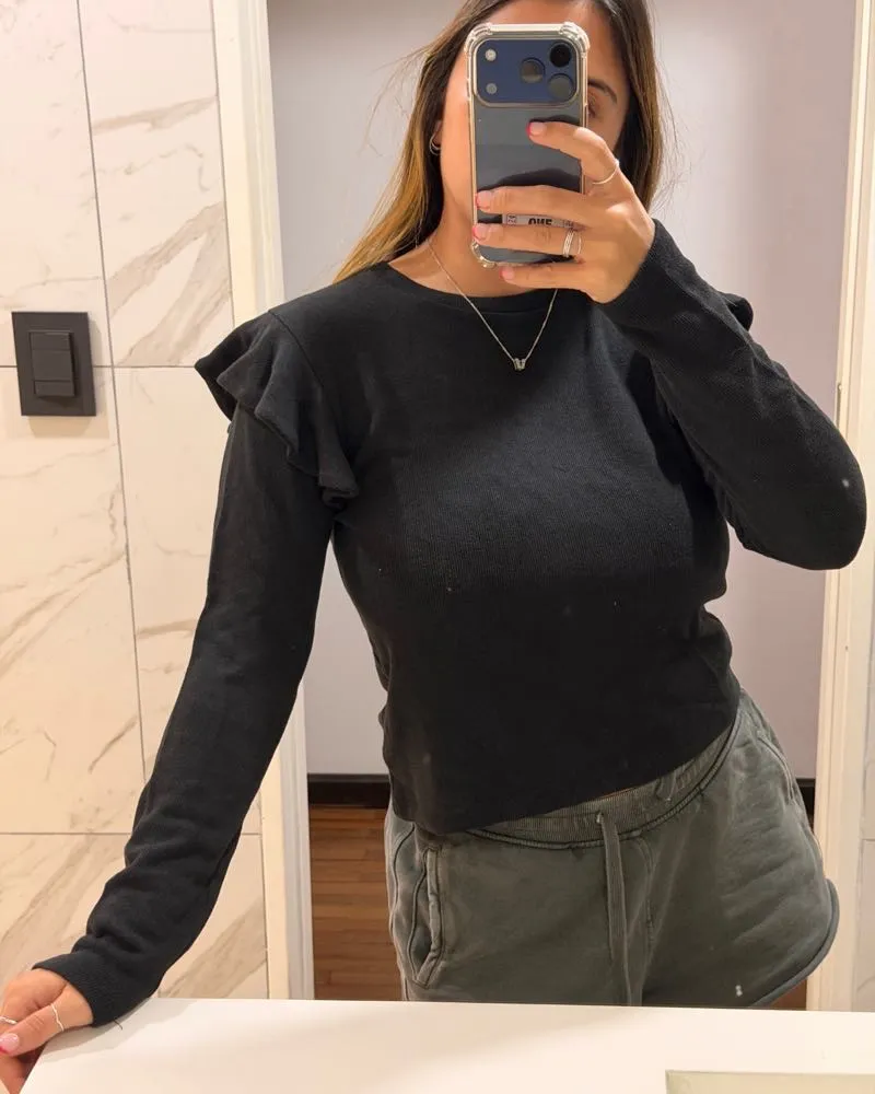 Remera negra de manga larga con detalles de volados en los hombros. Un básico canchero y cómodo para sumar a tu guardarropas.