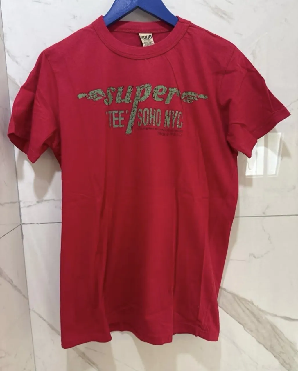 Remera roja de algodón con estampa "super tee soho nyc" en verde desgastado. Ideal para un look casual y urbano.