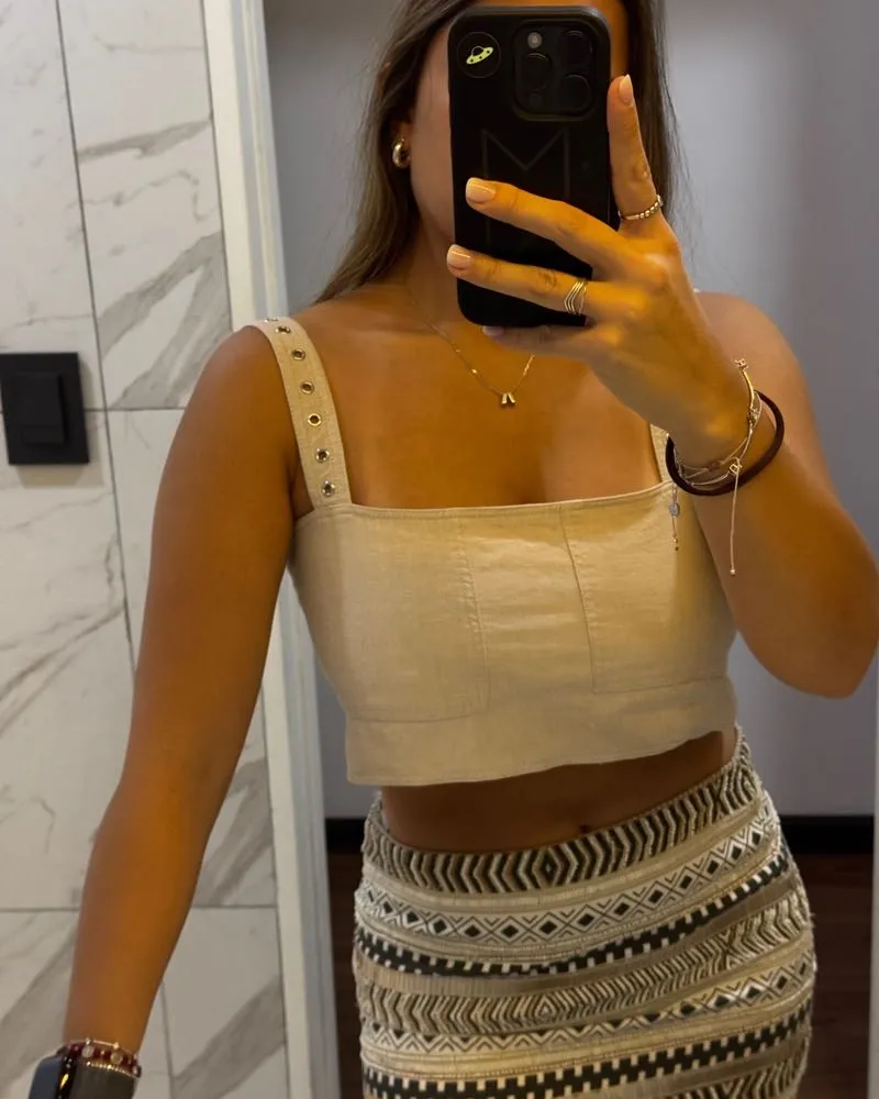 Top crop de lino color crudo con tiras regulables y detalle de ojales metálicos. Espalda con elástico fruncido y tiras cruzadas.