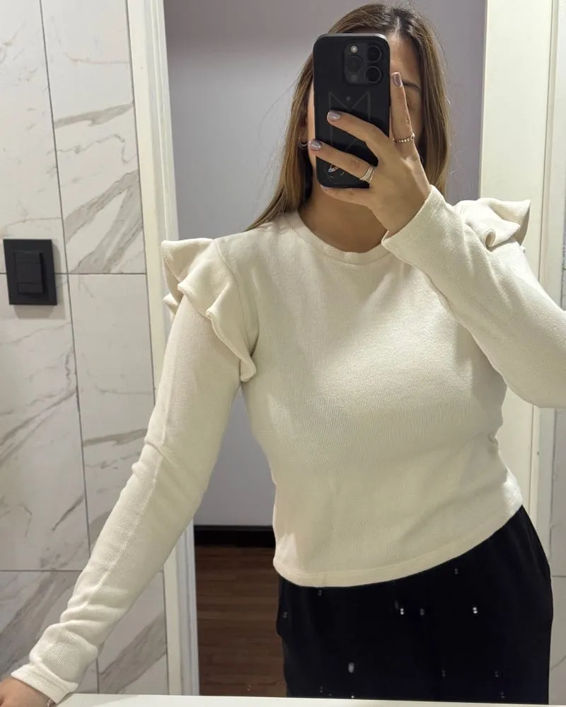 Remera de manga larga color crudo con detalles de volados en los hombros. Un básico canchero y delicado para sumar a tu guardarropas.