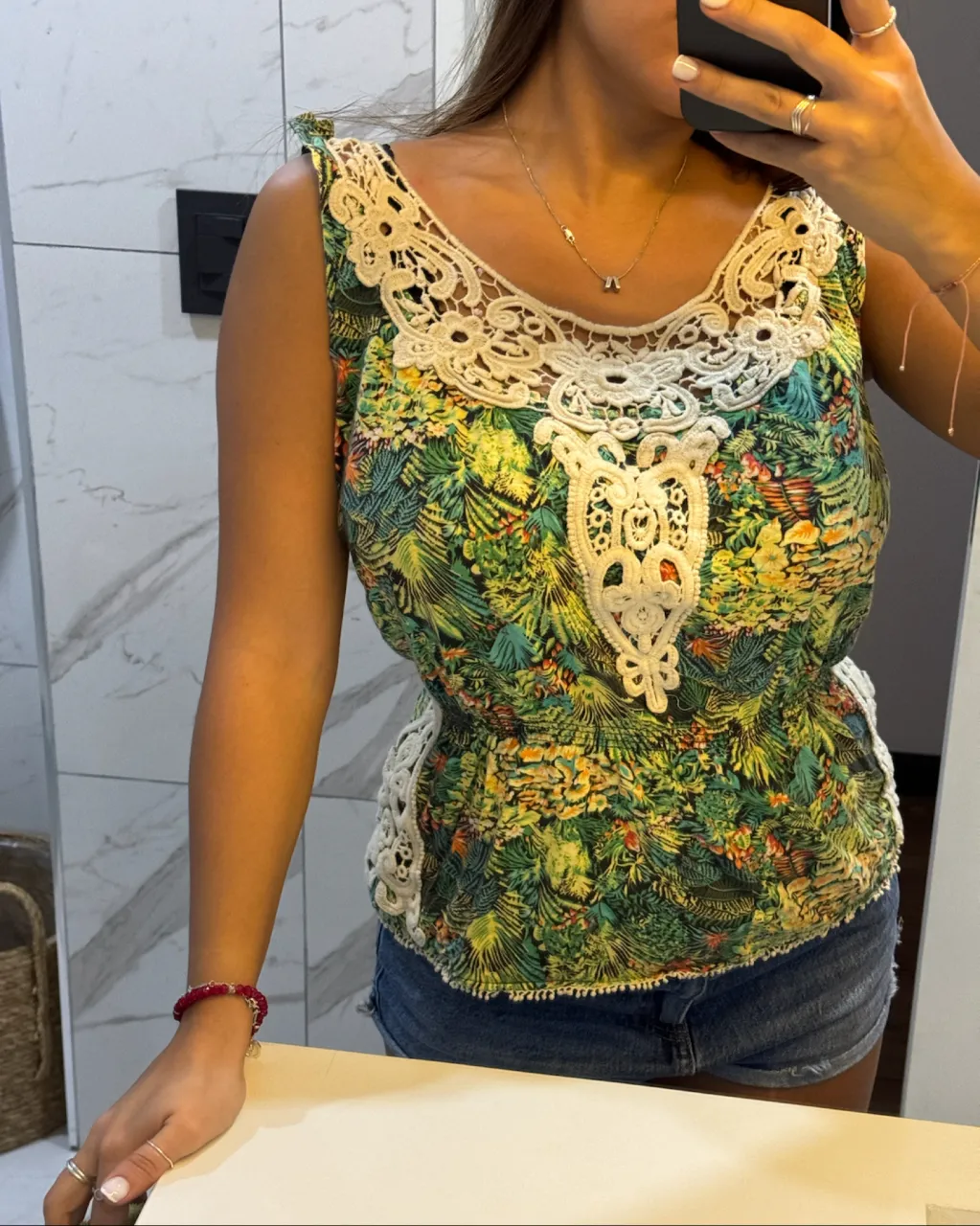 Musculosa estampada con motivos selváticos en tonos verdes y amarillos. Posee detalles de encaje blanco en el cuello y en los laterales. Escote redondo.