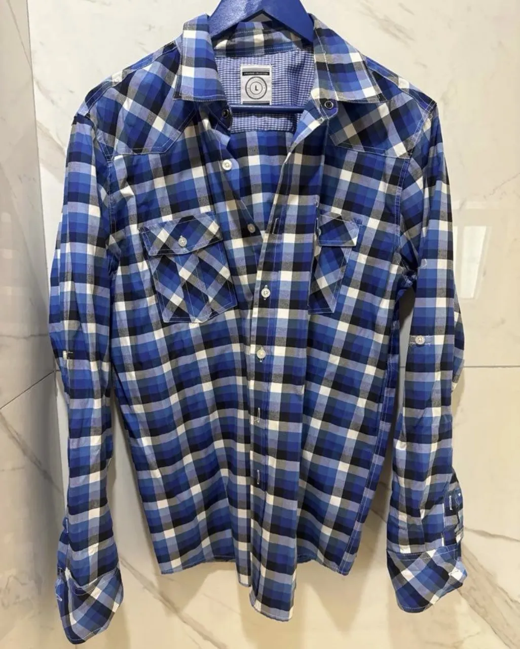Camisa de cuadros clásica en tonos azules, blancos y negros. Confeccionada en algodón, presenta un diseño de corte recto, cuello camisero y dos bolsillos en el pecho. Ideal para un look casual y moderno.